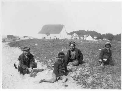 [Aleutian Islands? : 4 Indian boys seated on ground, buildings in…, 1899